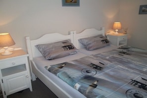 Ein Bett mit einem gemusterten Bettbezug, zwei Kissen, ein Nachttisch mit einer Lampe und einer Schublade.