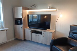 A modern living room with a flat-screen TV on a wooden cabinet, a leather chair, and a floor lamp. - Holiday apartment with 2 bedrooms (Langenhorn)