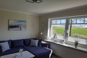 Ein Wohnzimmer mit einer Couch, einem Tisch, einem Gemälde, einem Fenster mit Blick auf ein Feld und einer Bootsdekoration.