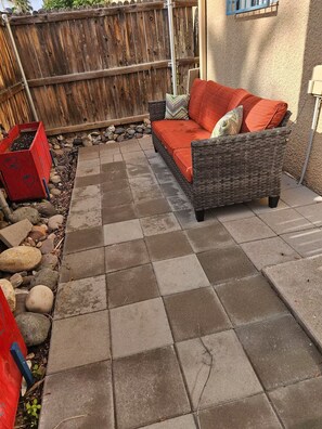 Eine Terrasse mit einem Korbsessel, einer roten Komposttonne und einem Holzzaun.