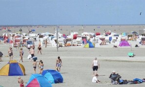 Ein Strand mit vielen Strandsonnenschirmen und Zelten, feinem Sand und blauem Himmel.