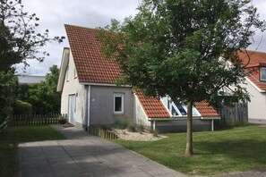 A residential house with a sloped roof, a garage, and a small garden area. - Holiday home with 1 bedroom (Scharendijke)
