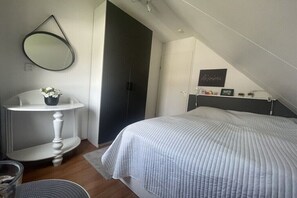 A bedroom with a bed, a white dresser, a round mirror, and a dark door. - Holiday home with 1 bedroom (Scharendijke)