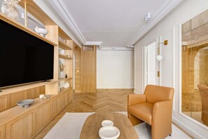 Ein modernes Wohnzimmer mit großem Flachbildfernseher, Holzregalen, einem Ledersofa und einem Fischgrätparkettboden.
