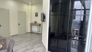 Una habitación con puerta corrediza de vidrio, una pequeña mesa con una silla y un televisor instalado en la pared.