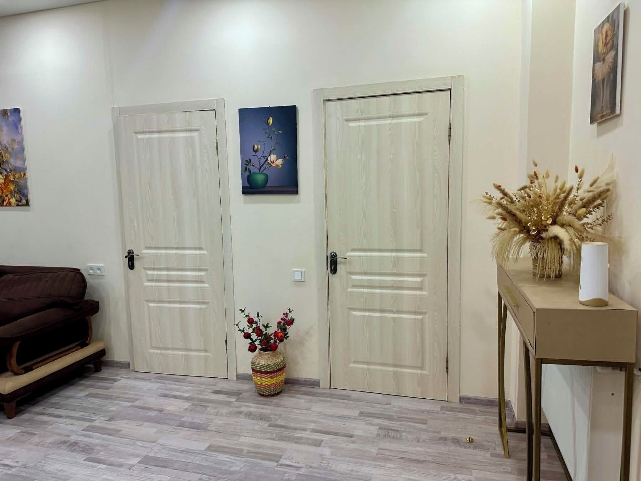 Une pièce avec deux portes fermées, un canapé marron, une petite table avec un vase et un tableau accroché au mur.
