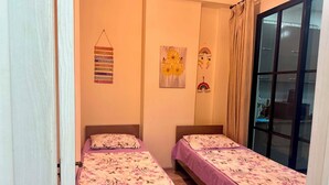 Una habitación con dos camas, una ventana con cortinas y adornos en la pared, incluyendo un cuadro de flores y un arcoíris.