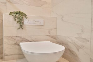 Ein modernes Badezimmer mit Toilette, Marmorfliesen und einer hängenden Pflanze.