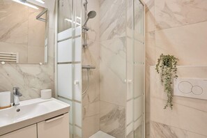 Ein Badezimmer mit Duschkabine aus Glas, Waschbecken mit Spiegel und Wandpflanze.