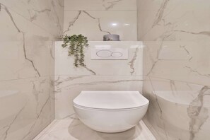Ein Badezimmer mit weißer Toilette, Marmorwänden, einer hängenden Pflanze und einem kleinen dekorativen Gegenstand an der Wand.