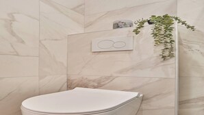 Ein modernes Badezimmer mit Toilette, einer Marmorwand, einer Duschkabine aus Glas und einem Topf mit Pflanze.