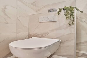 Ein modernes Badezimmer mit Toilette, einer Marmorwand, einer Duschkabine aus Glas und einem Topf mit Pflanze.