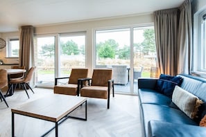 Ein modernes Wohnzimmer mit einer Couch, Sesseln, einem Couchtisch und großen Fenstern.