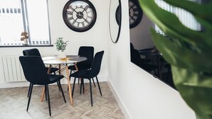 A dining area with a round table, black chairs, and two wall clocks. - Queensferry Collection - Residence 5 (Derby)
