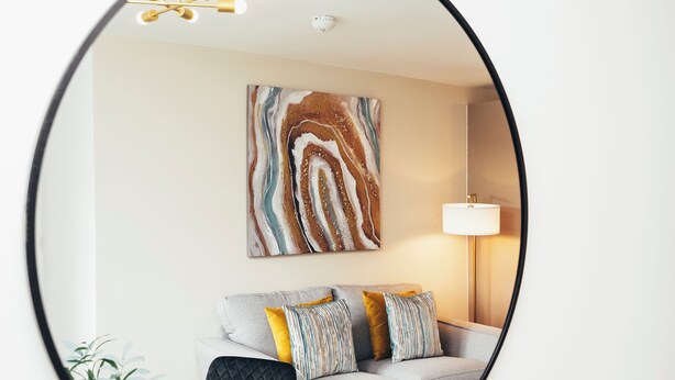A living room with a sofa, pillows, a lamp, and a wall-mounted abstract painting. - Queensferry Collection - Residence 5 (Derby)