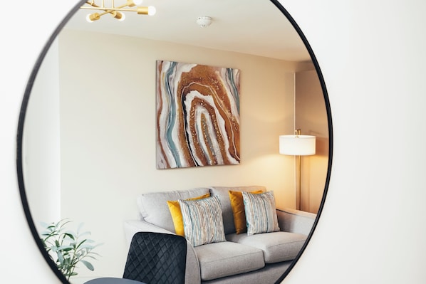 A living room with a sofa, pillows, a lamp, and a wall-mounted abstract painting. - Queensferry Collection - Residence 5 (Derby)