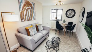 A modern living room with a sofa, coffee table, and dining area. - Queensferry Collection - Residence 5 (Derby)
