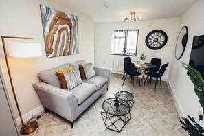 A modern living room with a sofa, coffee table, and dining area. - Queensferry Collection - Residence 5 (Derby)