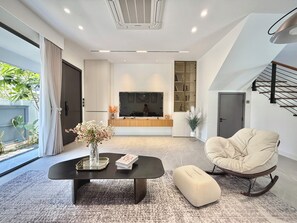 Ein modernes Wohnzimmer mit einem großen Fernseher, einem Sofa, einem Couchtisch und einem Sessel.