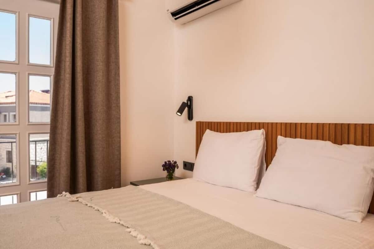 A hotel room with a bed, a nightstand, a wall-mounted phone, and a window with curtains.