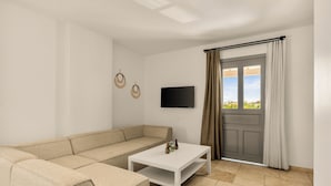A living room with a beige sectional sofa, a white coffee table, a flat-screen TV, and a door with curtains. - Molino Hotel (Çeşme)