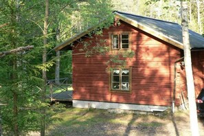 Eine kleine, einstöckige Holzhütte mit Satteldach, umgeben von Bäumen.