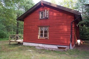 En rød træhytte med en lille veranda, et vindue og en dør.