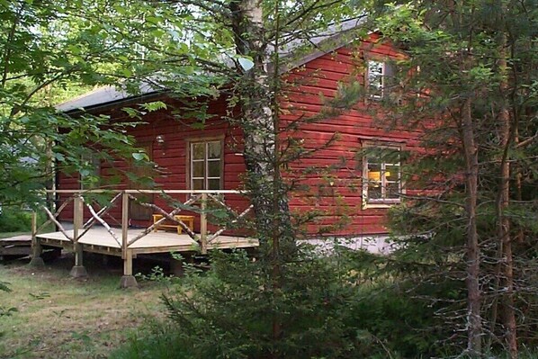 Eine rote Holzhütte mit einer Veranda, umgeben von Bäumen.