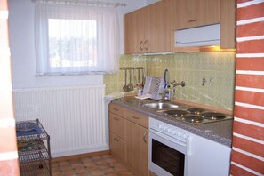 Eine Küche mit Holzausstattung, einem weißen Herd, einem Fenster mit weißem Vorhang und einer gefliesten Spritzschutzwand.