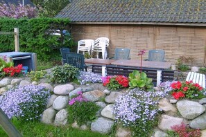 Ein Garten mit Tisch und Stühlen, umgeben von Steinen und Blumen.