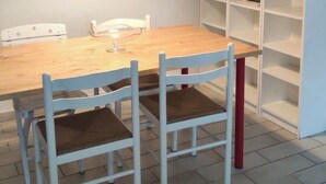 Zona de menjador amb taula de fusta i cadires blanques amb potes vermelles.