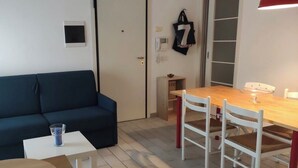 Un espai habitable reduït amb sofà, taula petita, taula de dinar amb cadires i un armari amb portes corredisses.