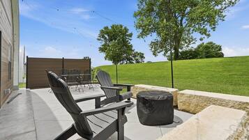 An outdoor patio with a table and chairs, a covered seating area, and a view of a grassy hill.