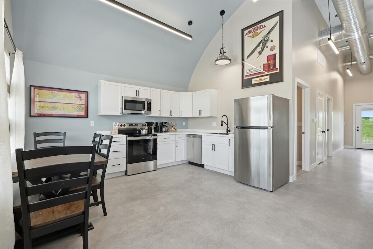 A kitchen with white cabinets, stainless steel appliances, and a dining area with a wooden table and chairs.