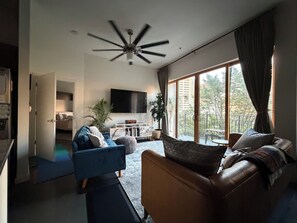 A modern living room with a ceiling fan, a TV, a sofa, a coffee table, and a view of the outdoors. - Studio Social - Steps from Stadium! & Pet Friendly (Atlanta)