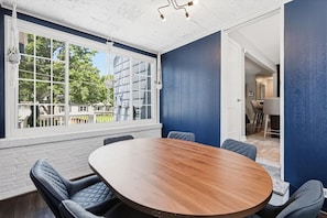Ett konferensrum med ett stort bord i trä och fyra stolar, ett stort fönster med utsikt över byggnader och en dörr som leder till ett annat rum.
