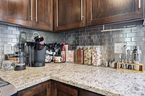 A kitchen with dark wooden cabinets, a granite countertop, and various kitchen appliances and utensils.
