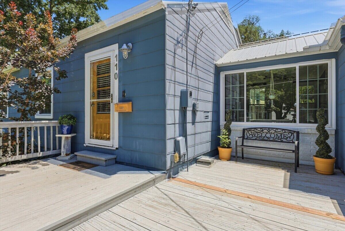 A small blue house with a wooden deck, a bench, and a welcome sign.