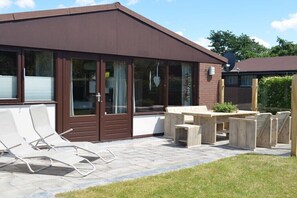 Ein modernes Haus mit Terrasse, einer Schiebetür und einem Holztisch mit Stühlen.