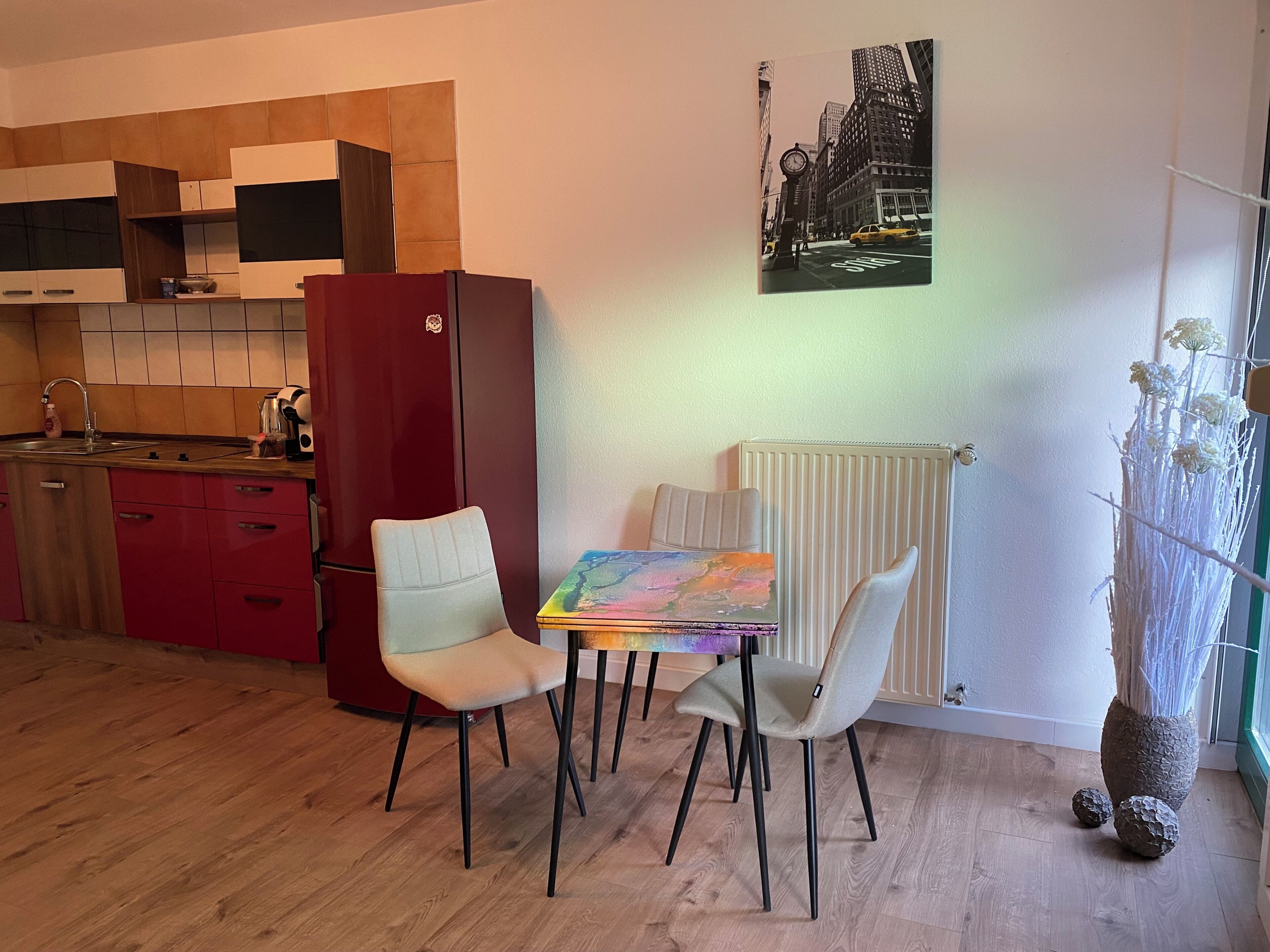 Eine moderne Küche mit einem roten Kühlschrank, einem Esstisch mit zwei Stühlen und einem Stadtbild an der Wand.