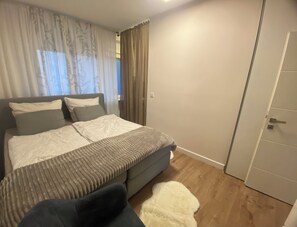 A bedroom with a bed, a chair, a white rug, and a door. - Cosy apartment in Reimsbach perfect for your stay (Beckingen)