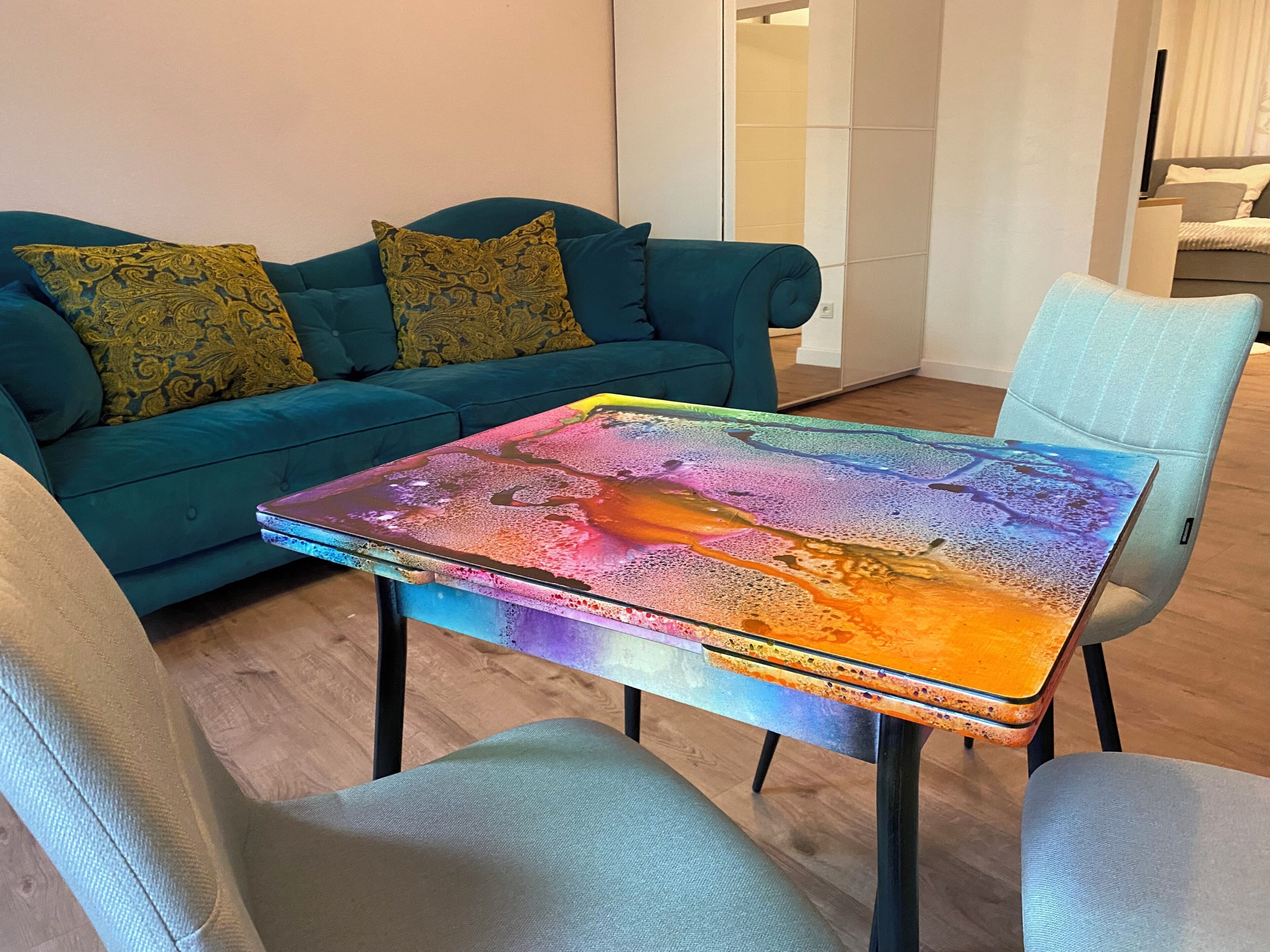 Een smaragdgroene bank met geknoopte kussens, een kleurrijke tafel en een lichtblauwe stoel in een moderne woonkamer.