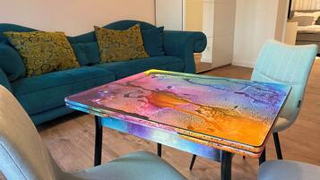 Een smaragdgroene bank met geknoopte kussens, een kleurrijke tafel en een lichtblauwe stoel in een moderne woonkamer.