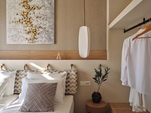 A modern bedroom with a bed, pillows, a hanging light, a wall-mounted artwork, a bedside plant, and a wooden headboard.