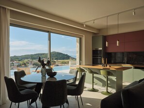A modern kitchen with a large island, dining area with chairs, and a view of a body of water and hills.