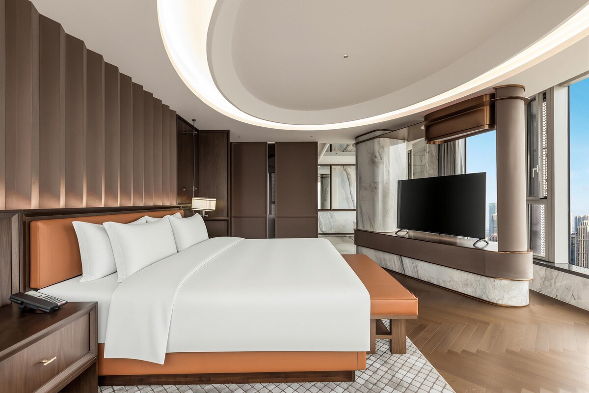 Quarto de hotel moderno com uma cama grande, televisão de tela plana e vista para a cidade.