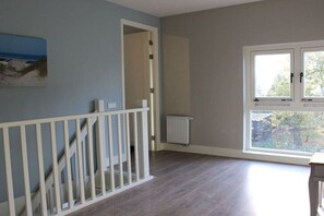 Ein Zimmer mit Holzboden, weißer Handläufung, Heizkörper und Fenster mit Blick auf Bäume.