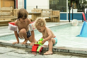 Kinder spielen am Pool, mit einer Rutsche und einem Ball im Hintergrund.