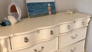 A white dresser with ornate handles, a small mirror, and a painting of a beach scene.