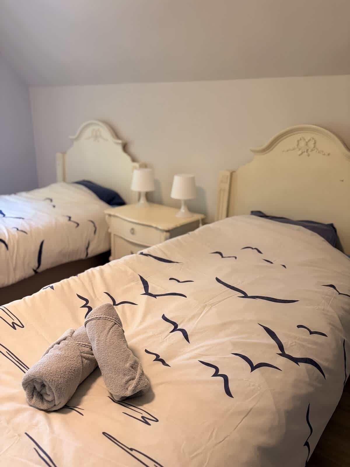 Habitación de hotel con dos camas, cada una con cabecero, mesitas de noche con lámparas y una toalla sobre la cama.